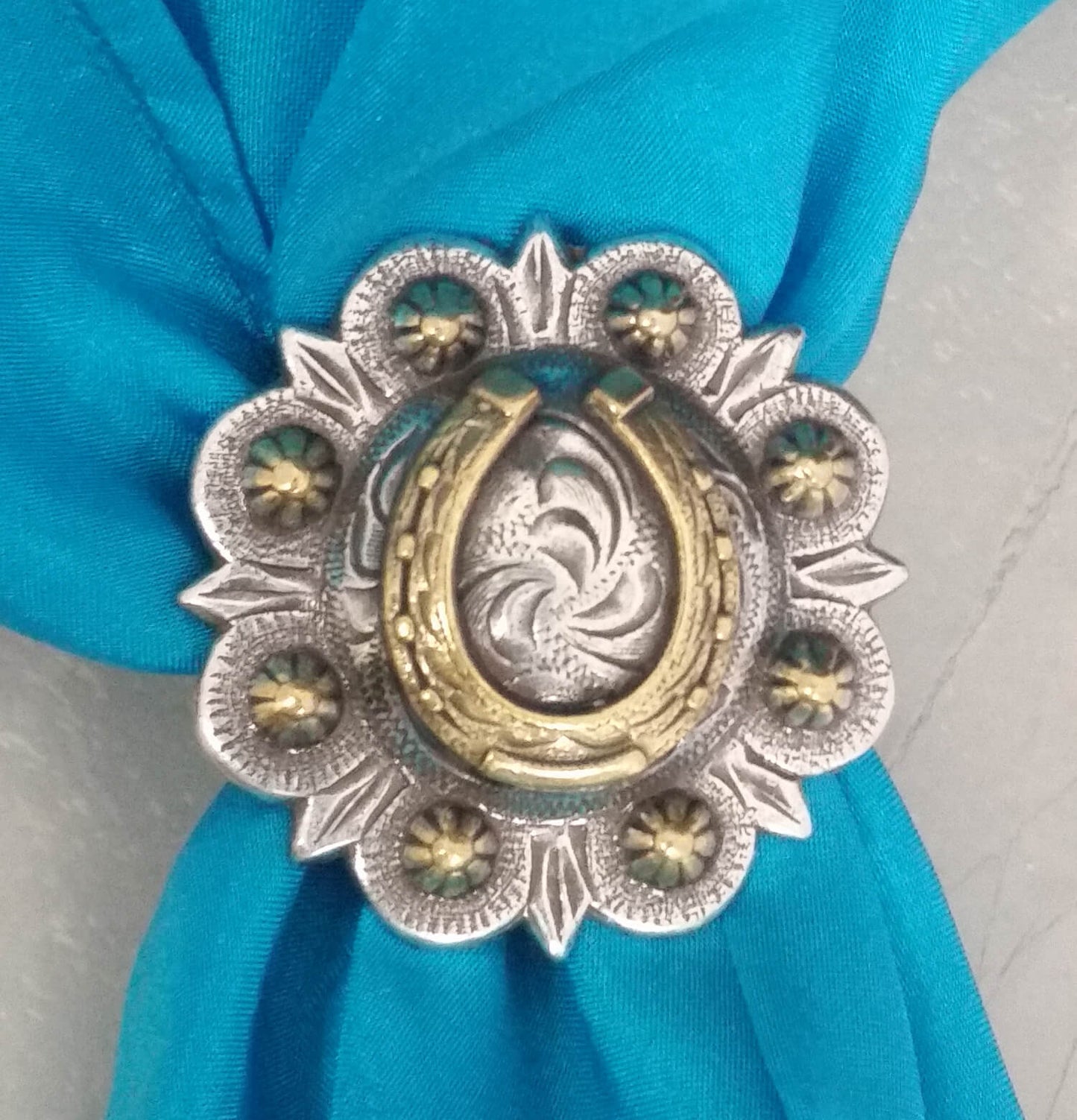 Horseshoe Concho Western Scarf Slide featuring a brass horseshoe on a berry concho with etched design on a blue scarf.