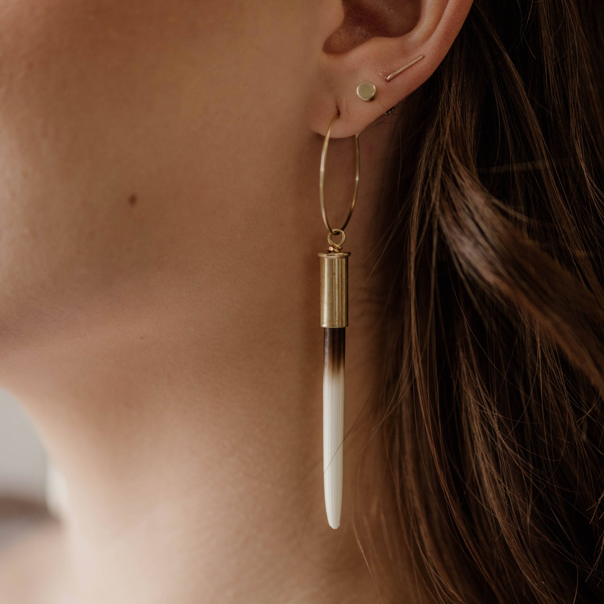 Close-up of a woman's ear wearing gold hoop earrings with a long, thin pendant.
