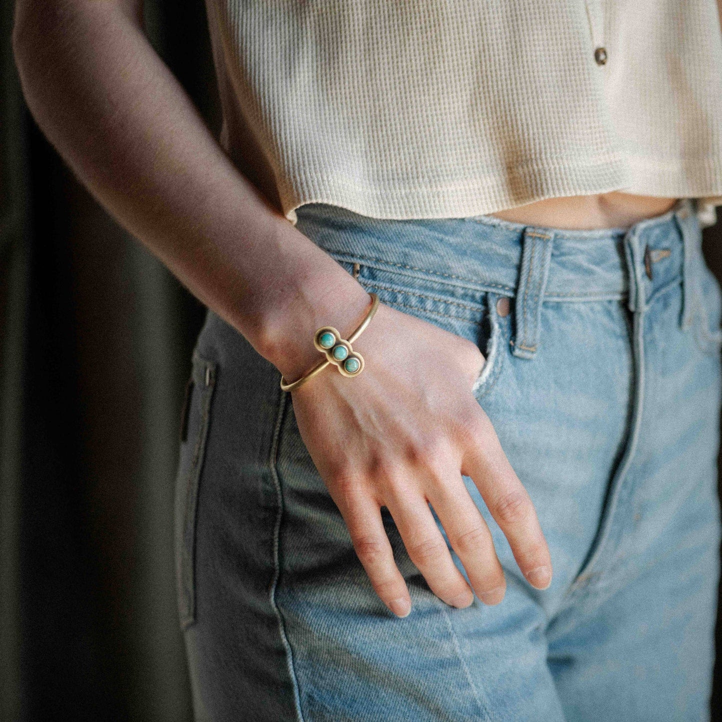Person wearing a gold bracelet with green stones on a blurred background