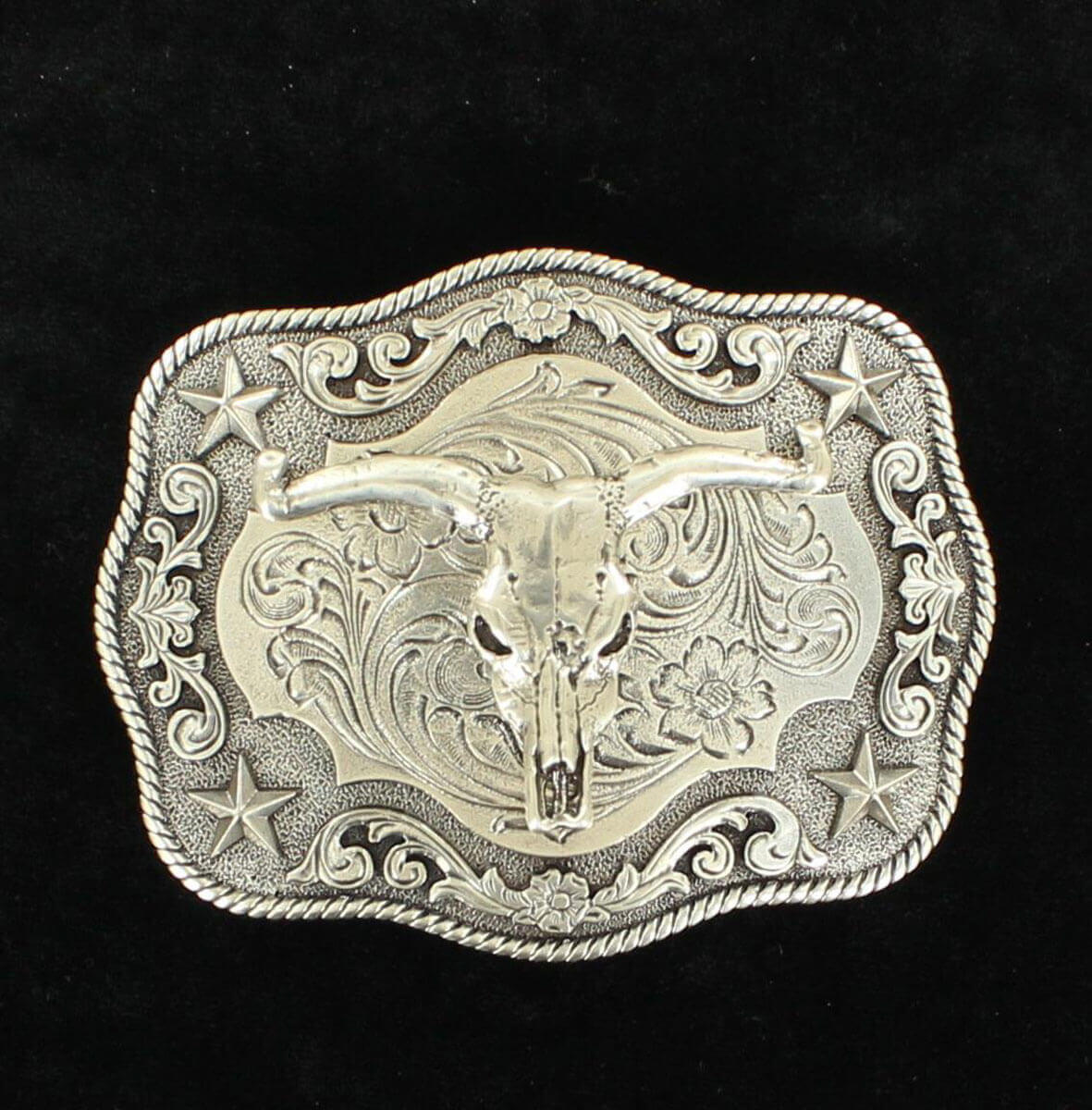 An antique silver belt buckle with a steer skull motif in the center, set against a black background with a scroll pattern.
