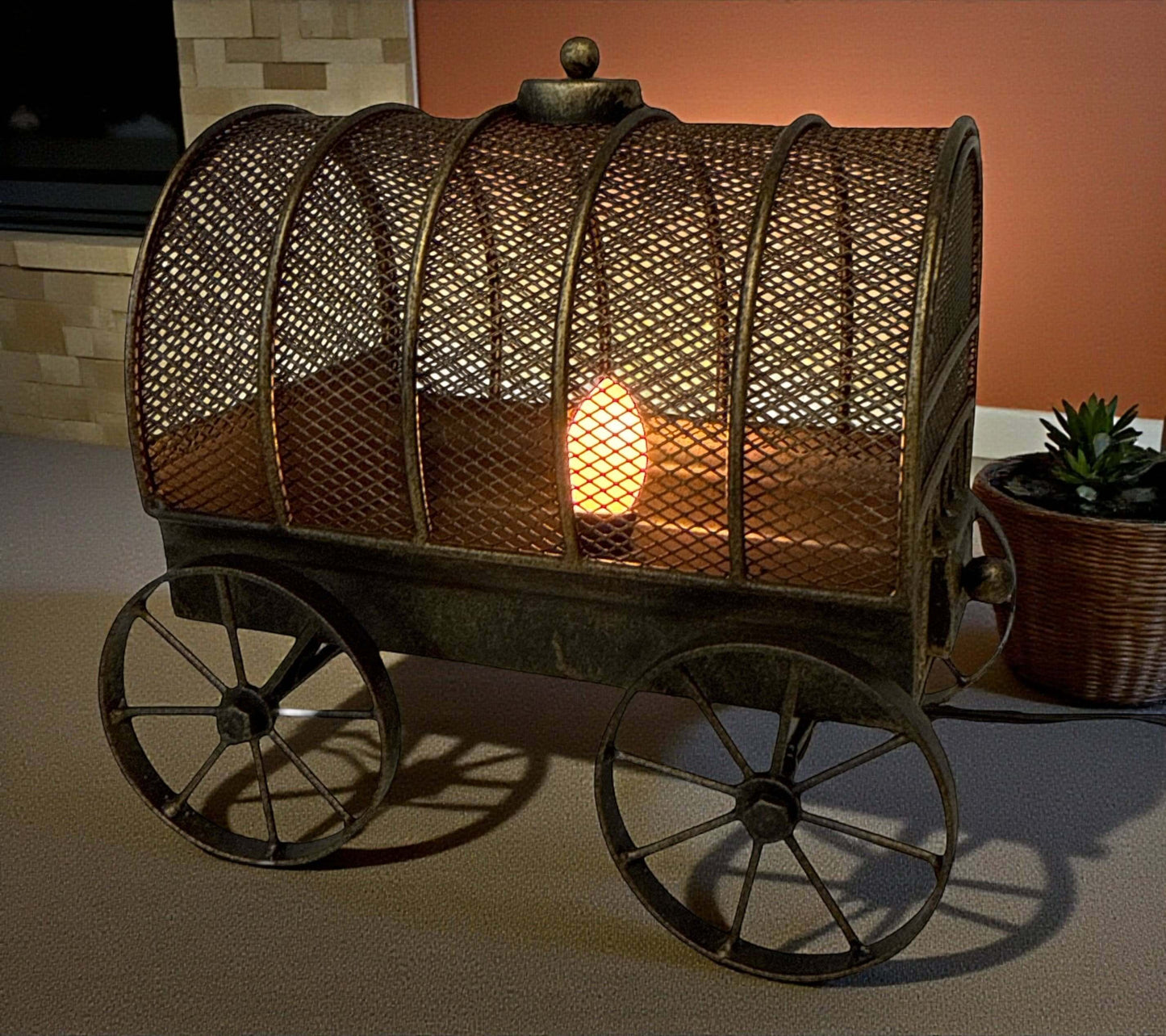 Decorative metal cart with a light bulb inside, resembling a wagon, on a neutral background.