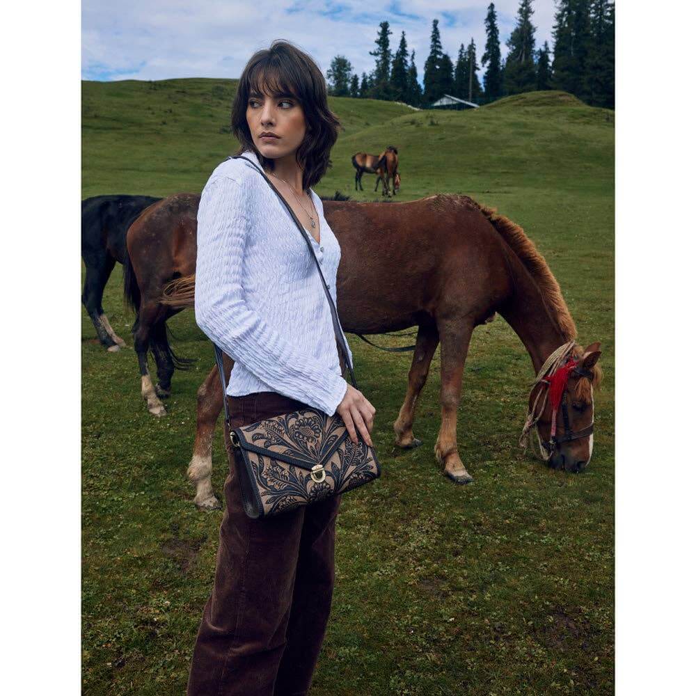 Model wearing Lark Hand Tool Ladies Western Purse in a scenic field with horses.
