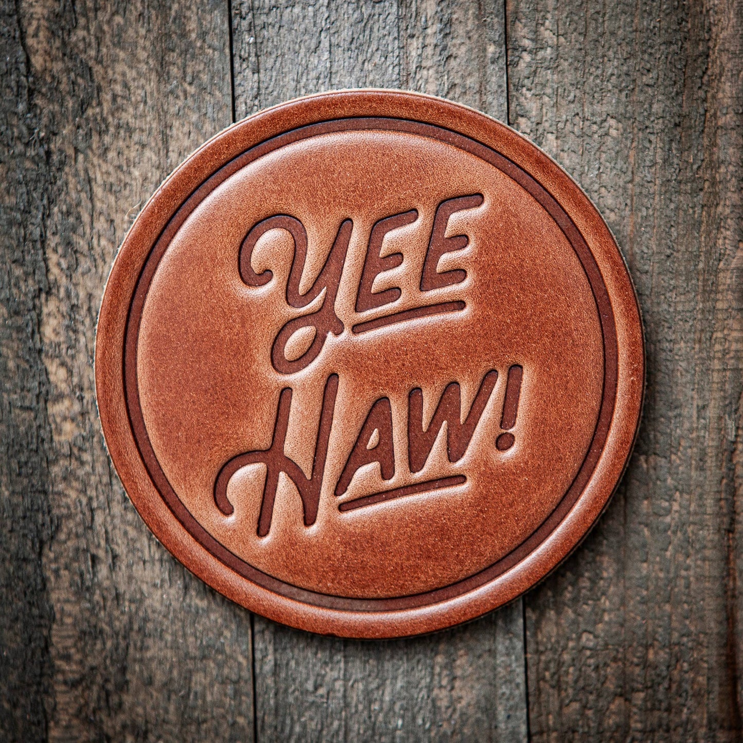 Round leather coaster with 'Yee Haw!' text on a wooden background