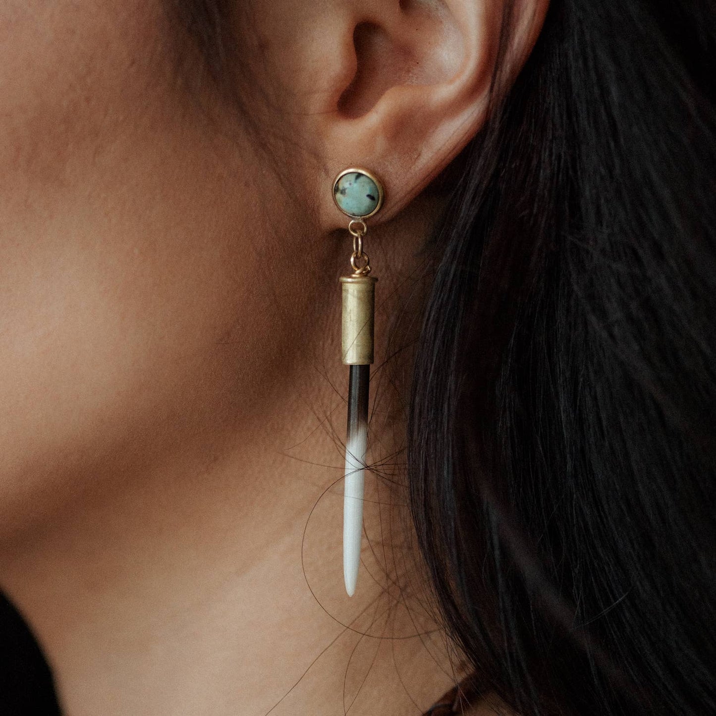 Close-up of an earring with a gold and turquoise stone on a blurred background