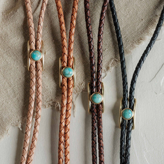 Four braided leather bolo ties with turquoise stones on a textured surface