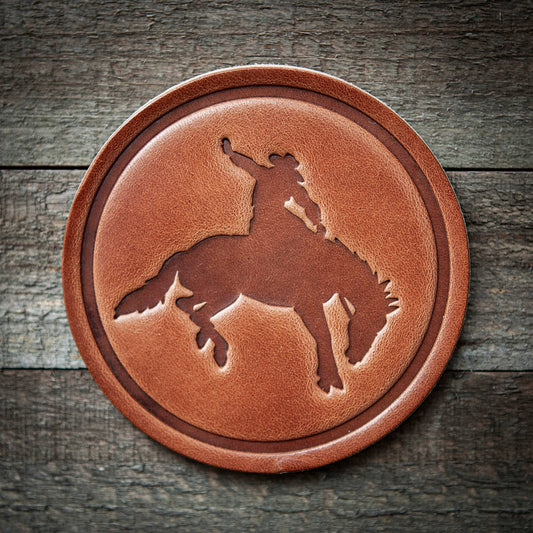 Round leather coaster with a horse and rider design on a wooden background