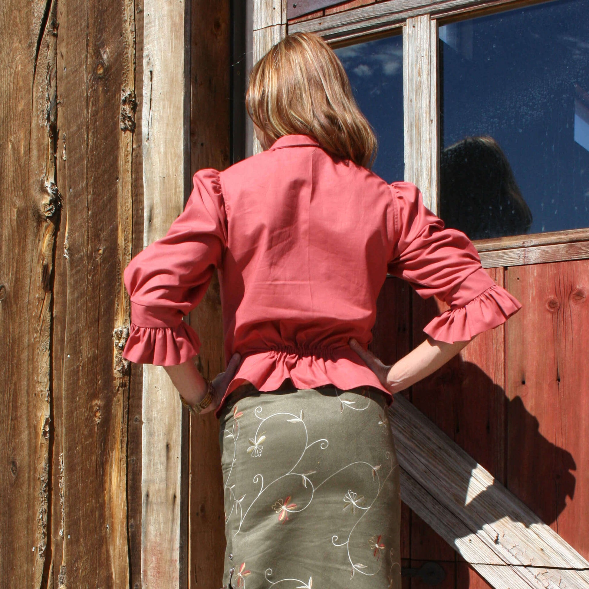 Back view of a ladies angel blouse with ruffled sleeves, paired with a floral skirt, against a rustic wooden backdrop.