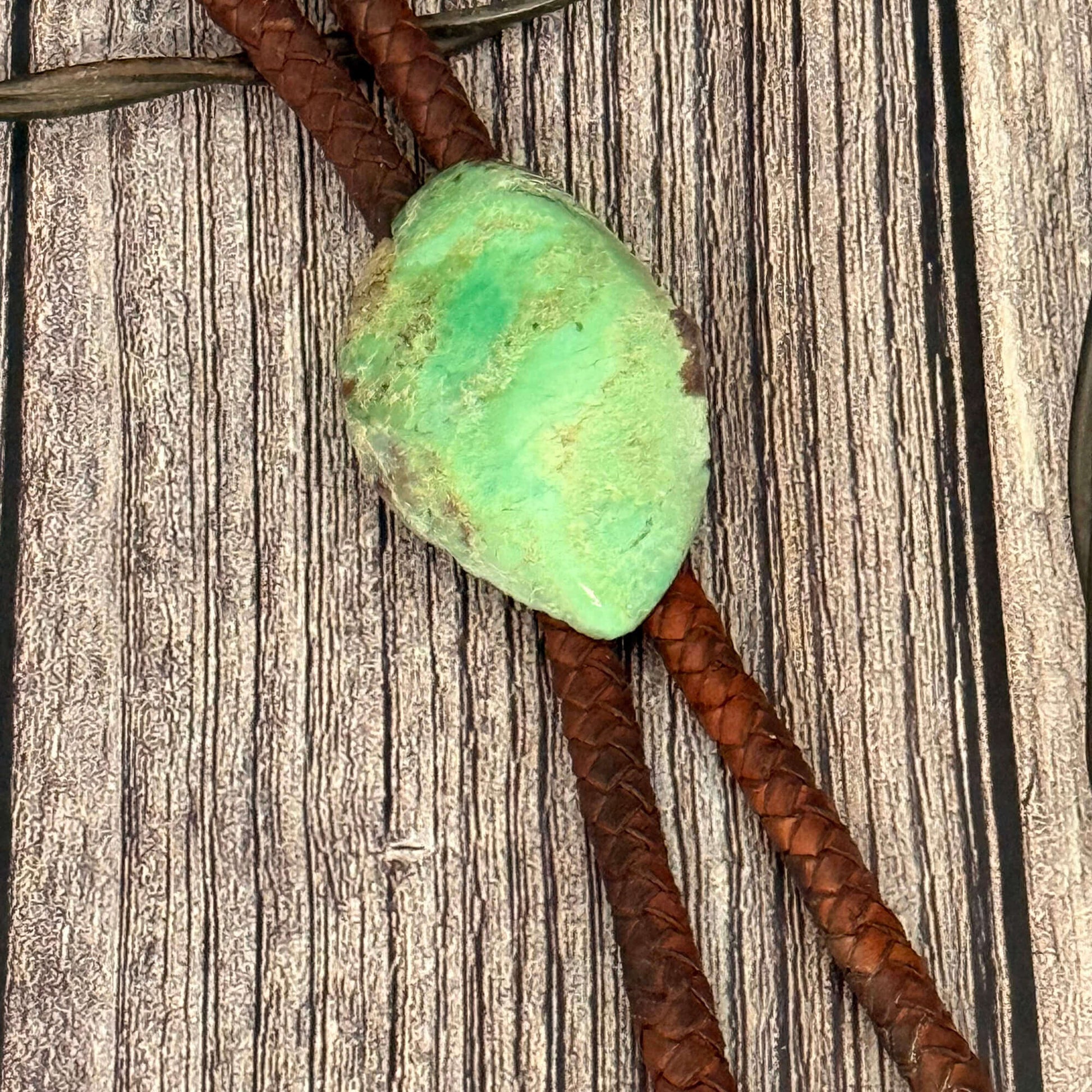 Turquoise stone on a brown leather cord against a wooden background