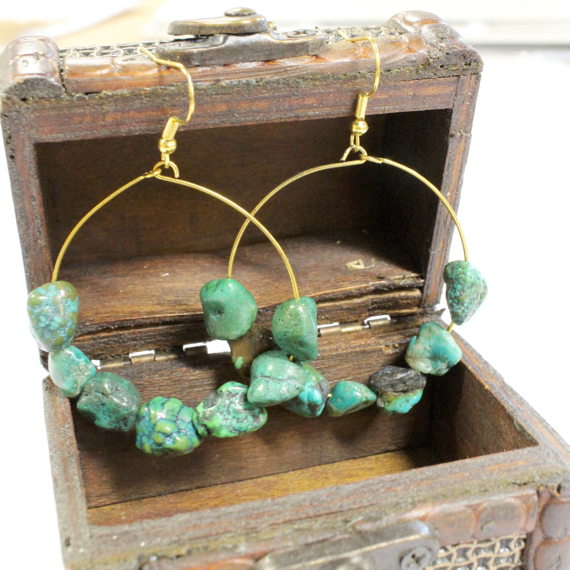 Gold hoop earrings with irregular green turquoise-like beads, displayed inside an open rustic wooden box.