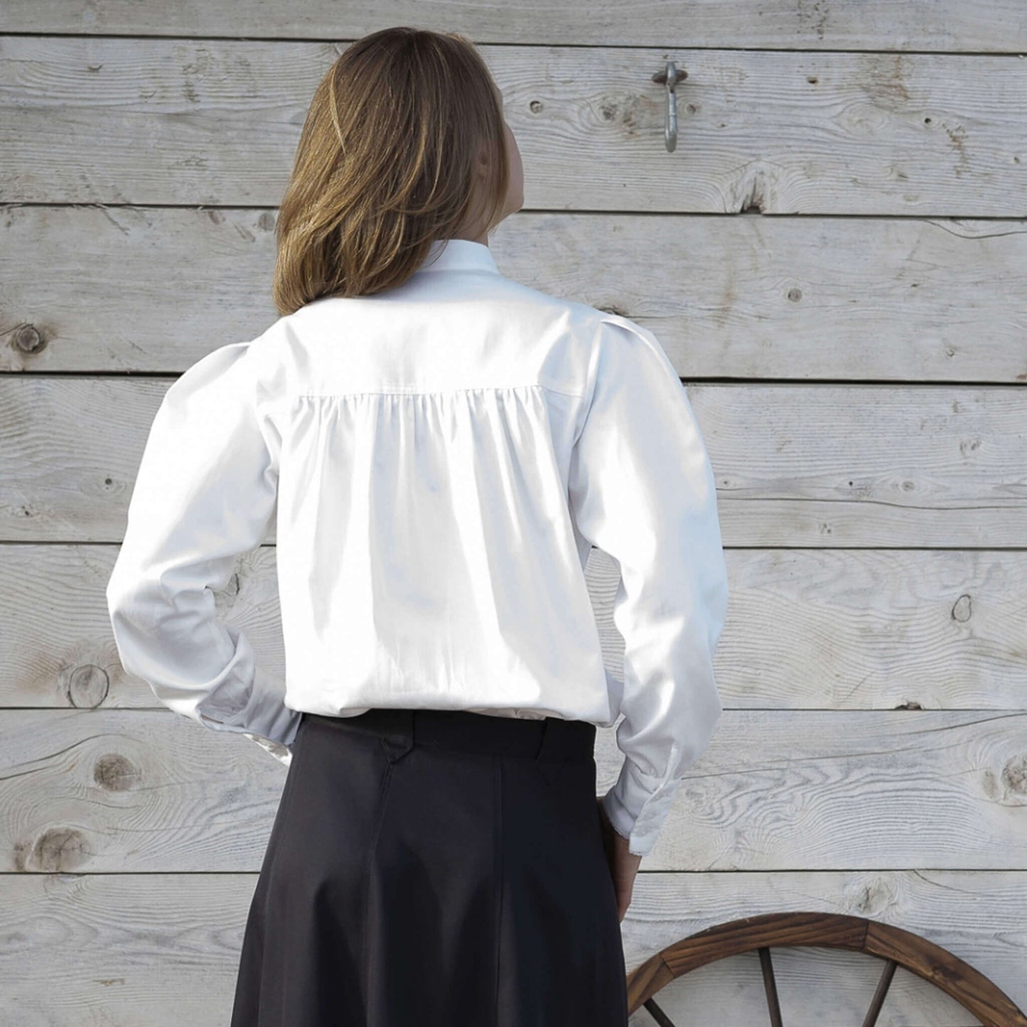 Back view of a woman wearing a Belle Western Victorian Blouse with puffed sleeves against a rustic wooden backdrop.