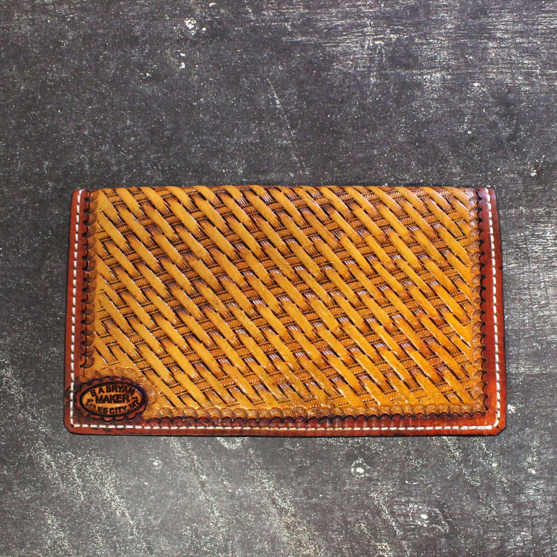 Brown leather cardholder with woven pattern on a dark textured surface