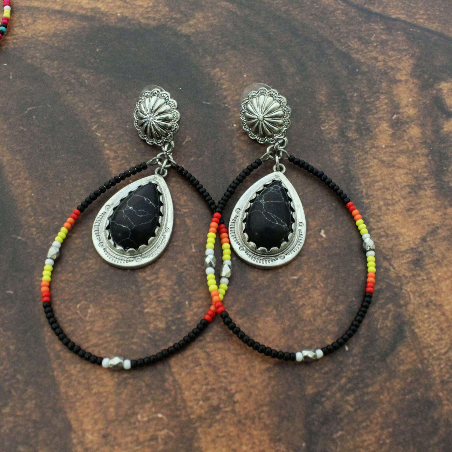 Pair of earrings with black stones and colorful beads on a wooden surface