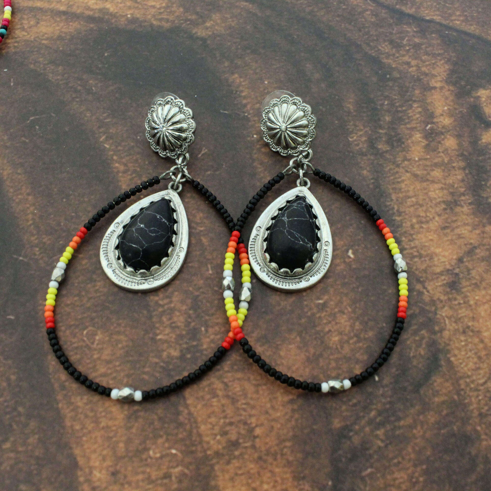Pair of earrings with black stones and colorful beads on a wooden surface