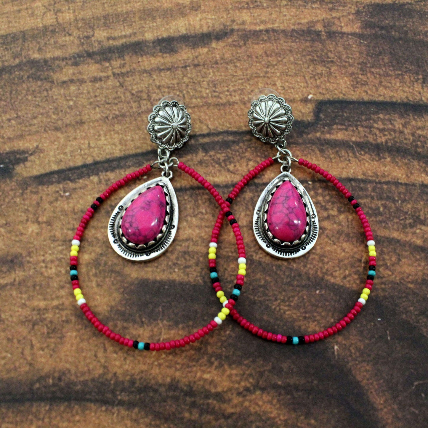 Pair of earrings with pink teardrop stones and red beaded loops on a wooden surface