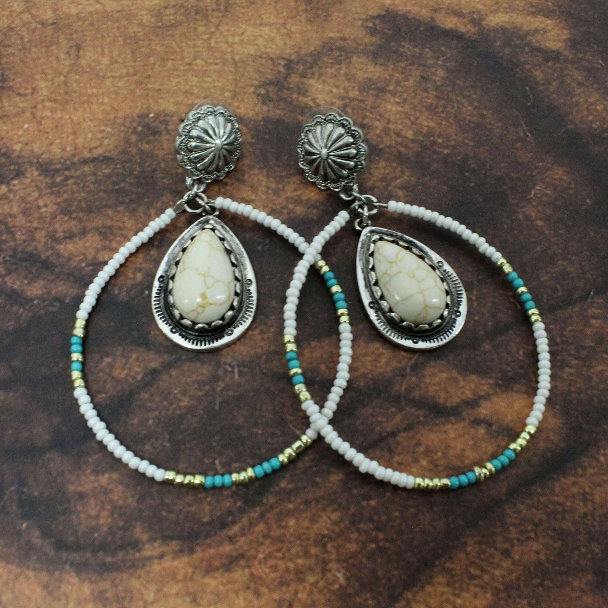 Pair of silver earrings with teardrop-shaped stones and beaded accents on a brown background