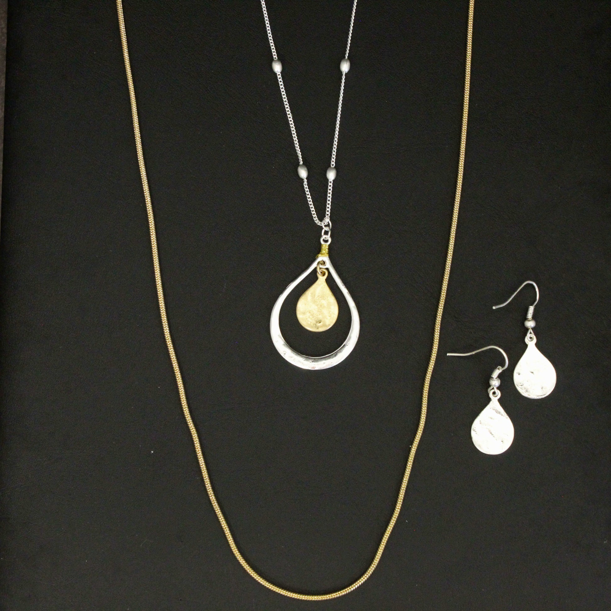 Gold necklace with a teardrop pendant and matching earrings on a black background