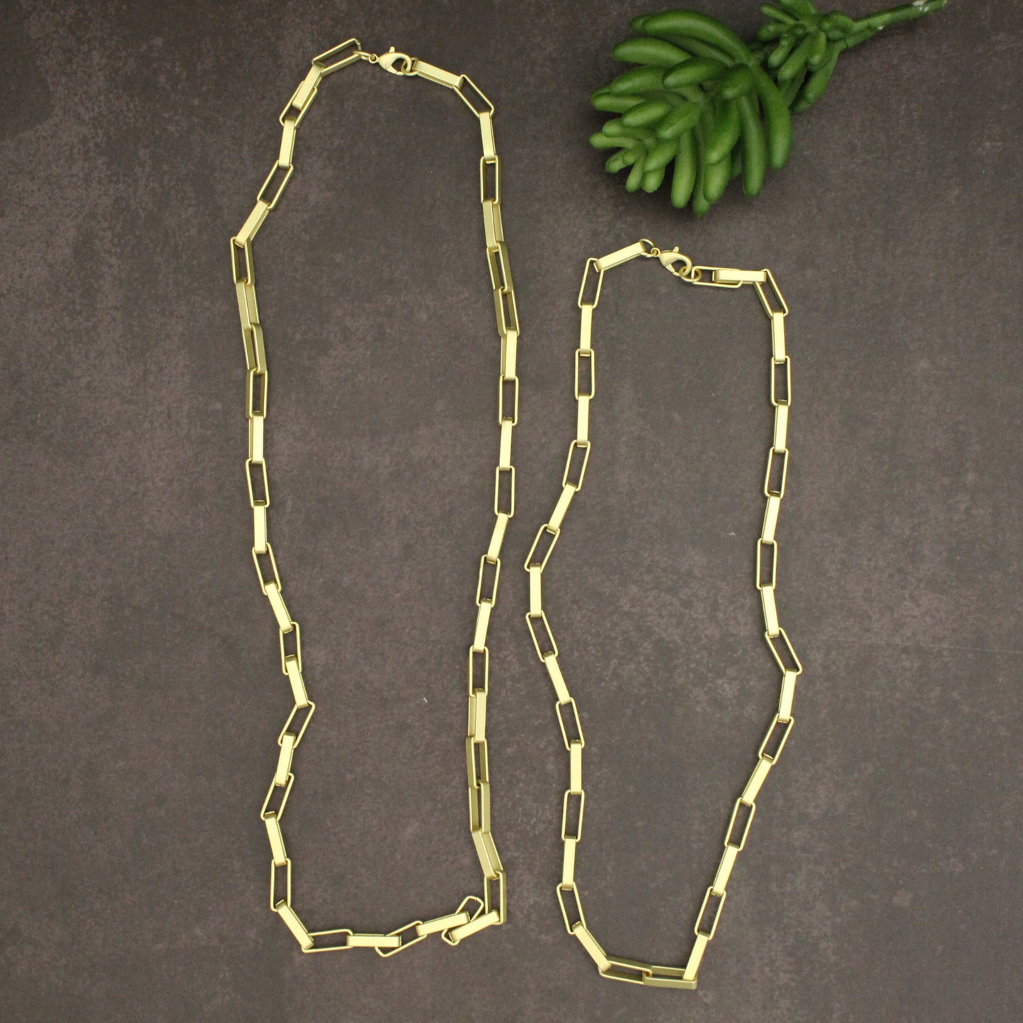 Gold chain necklace on a dark surface with green leaves.