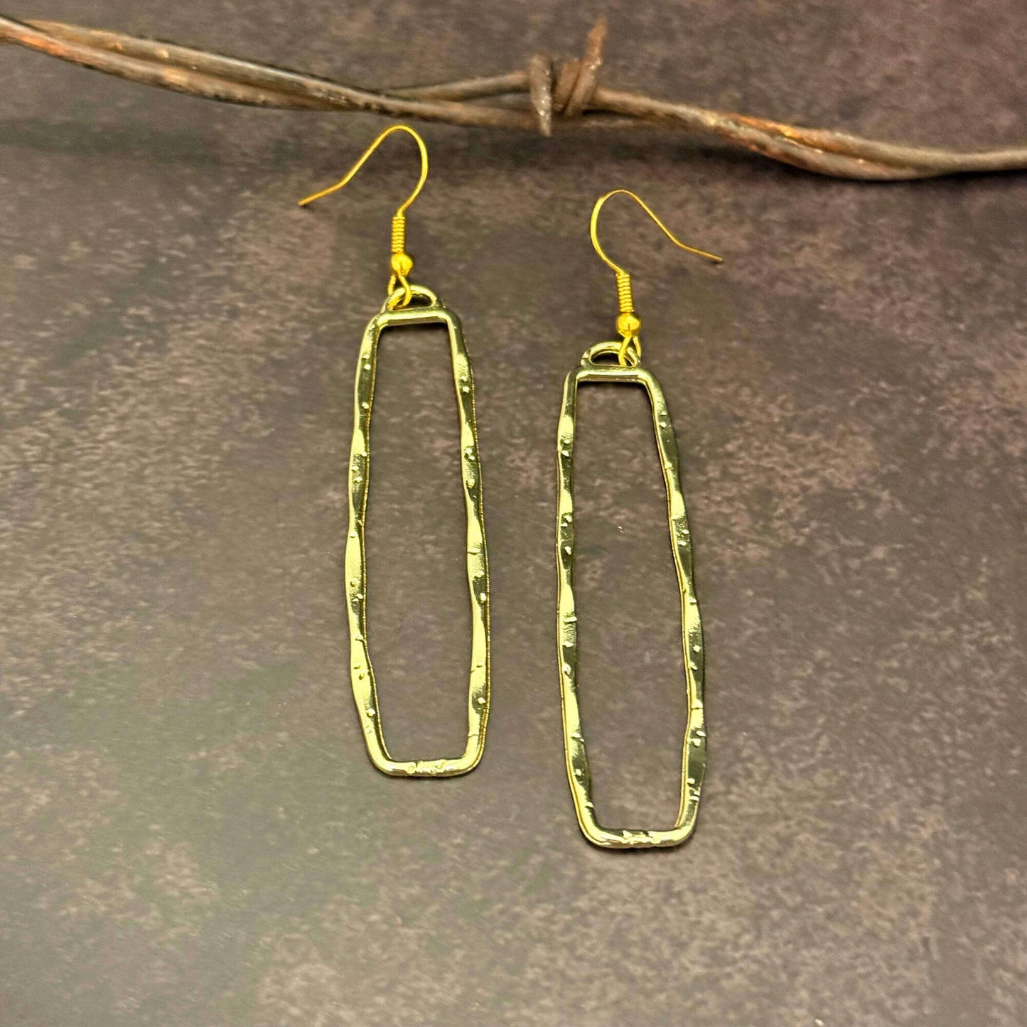 Gold Dangle Rectangle earrings on a textured brown surface