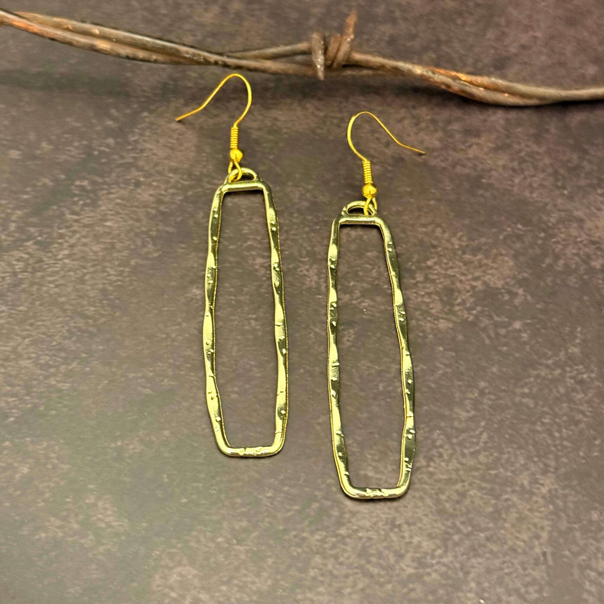 Gold Dangle Rectangle earrings on a textured brown surface