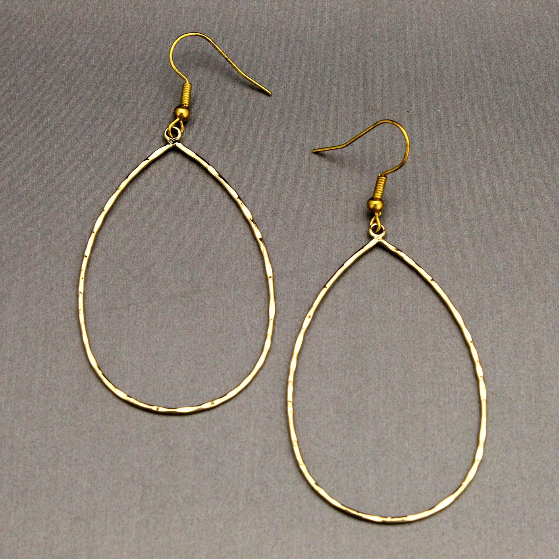 A pair of gold-tone teardrop hoop dangle earrings with textured, hammered edges and fishhook backings, displayed on a neutral gray background.