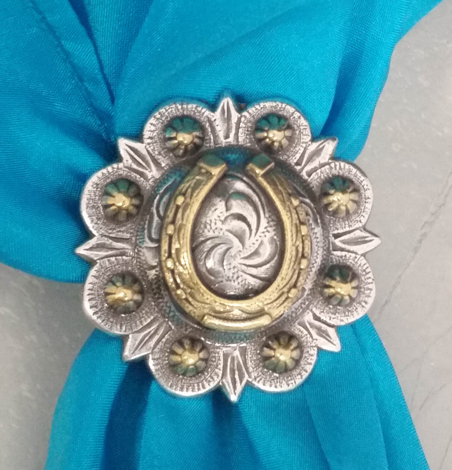 Horseshoe Concho Western Scarf Slide featuring a brass horseshoe on a berry concho with etched design on a blue scarf.