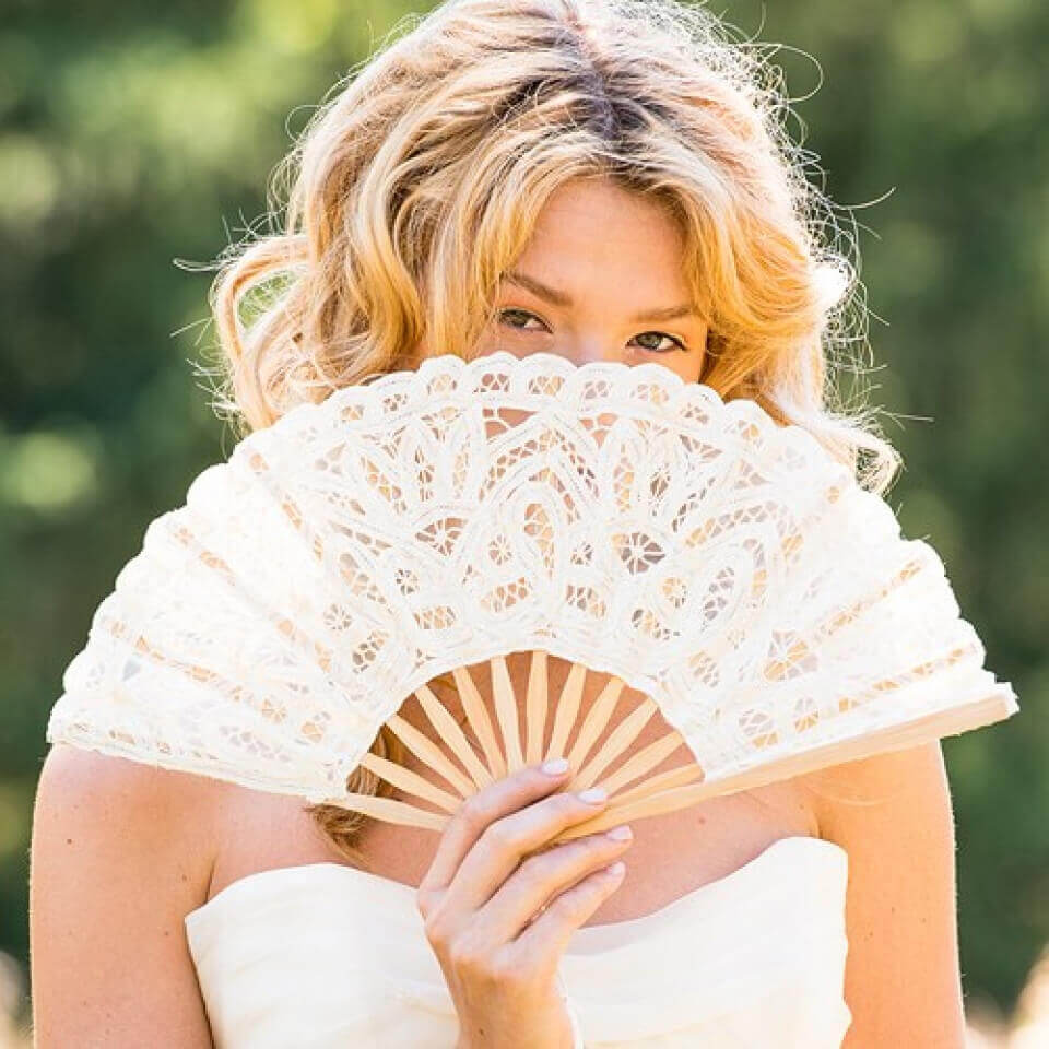 Woman holding a lace fan outdoors with a blurred green background