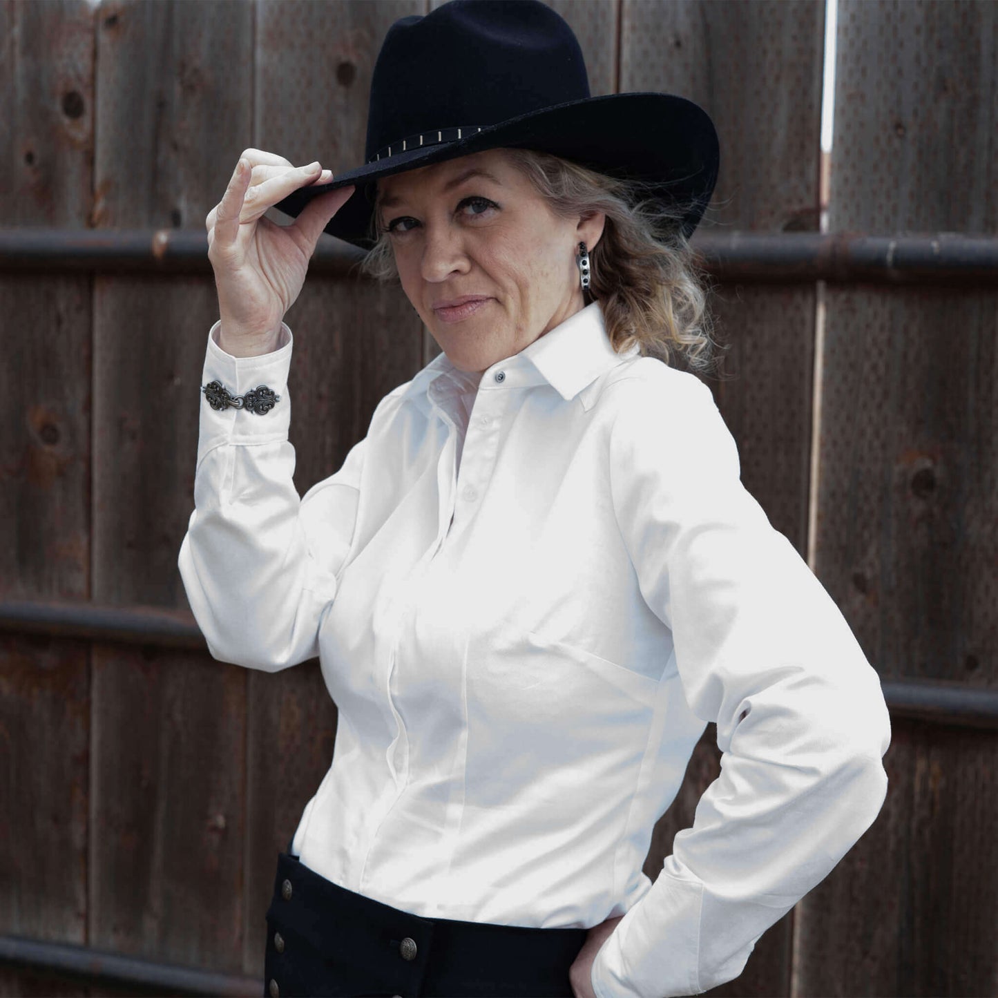 Model wearing a white Western Riding Blouse with unique cuff details and a black cowboy hat, against a rustic wooden background.