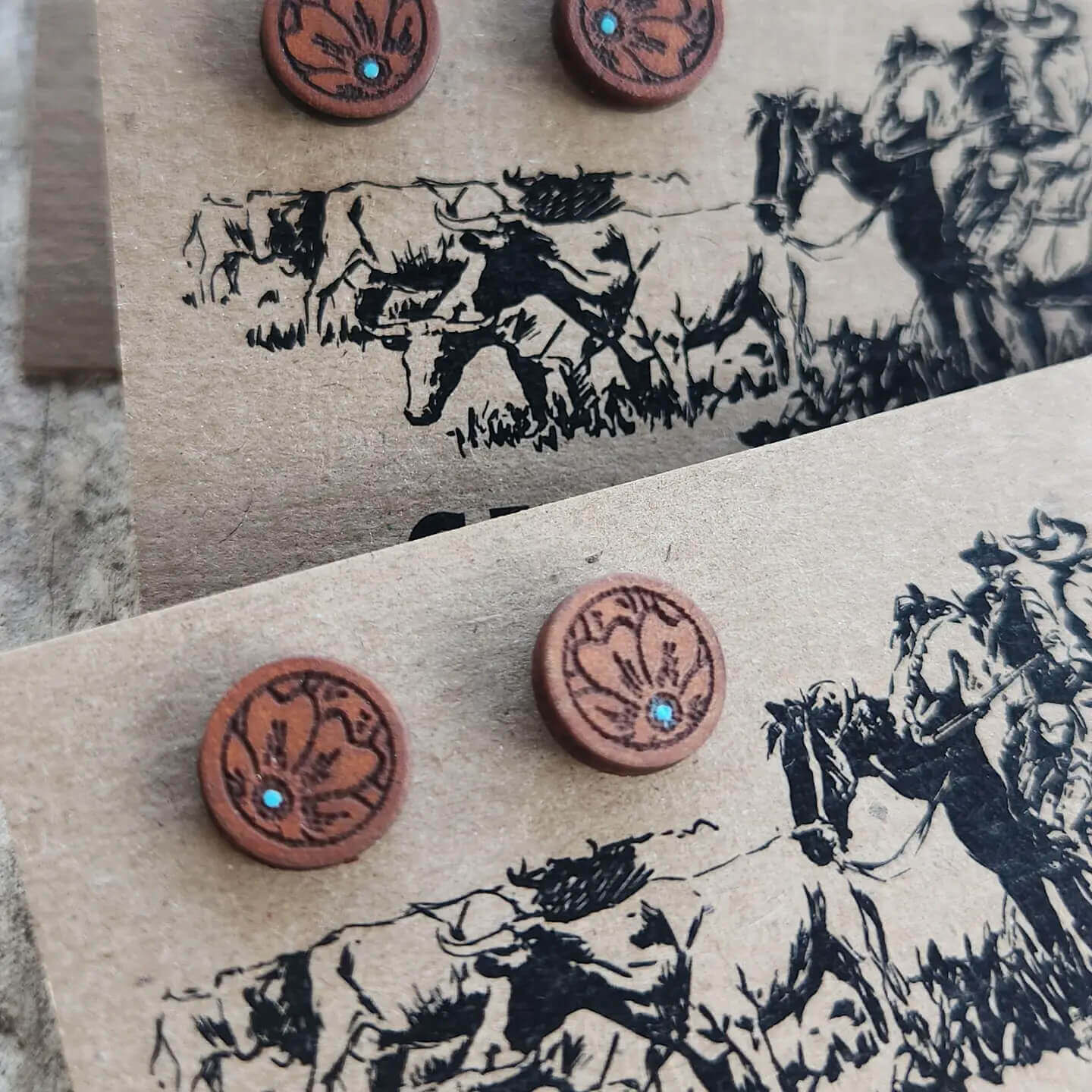 Pair of round leather earrings with embedded stones on a card with horse illustrations.