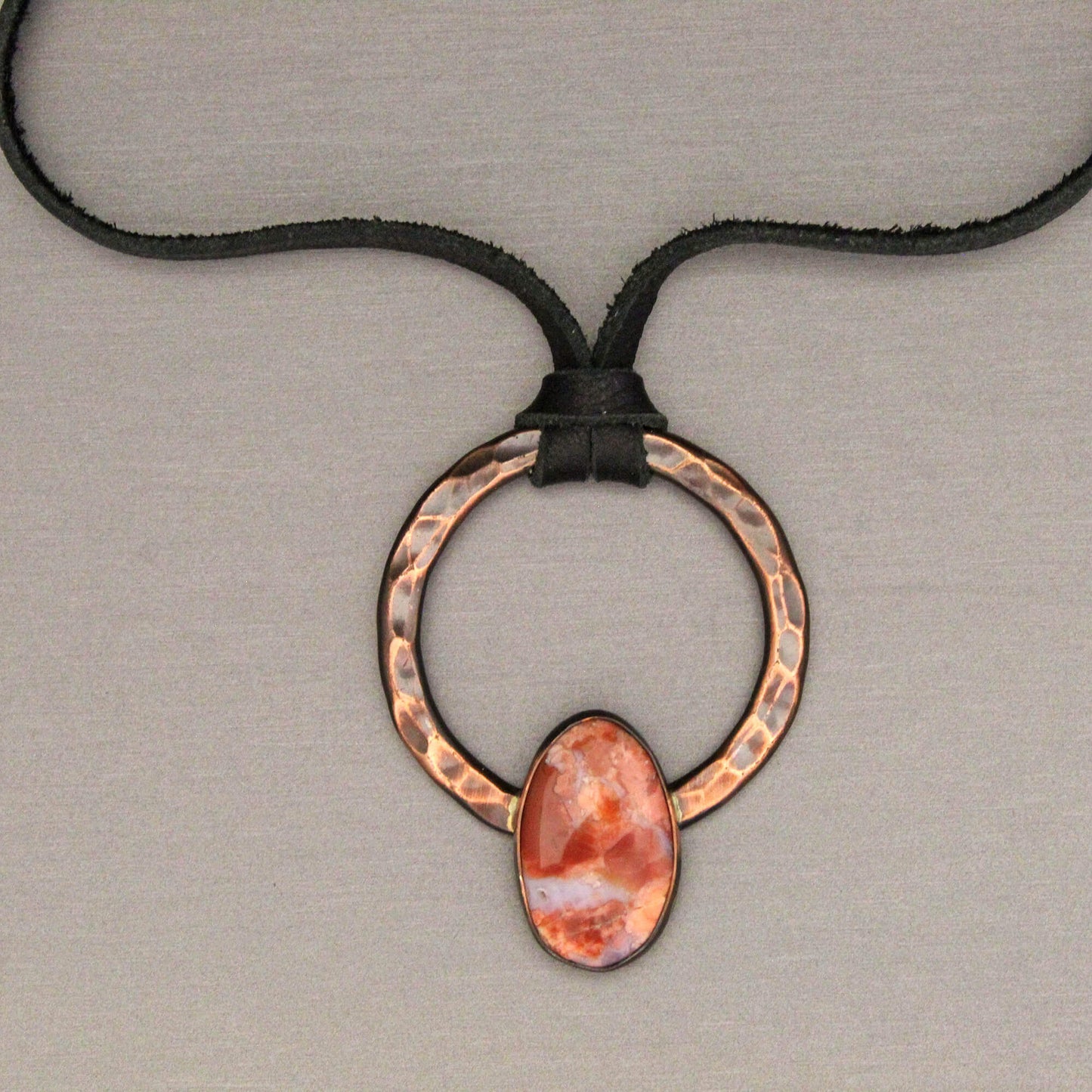 Necklace with a copper ring and cotton candy agate stone pendant on a neutral background