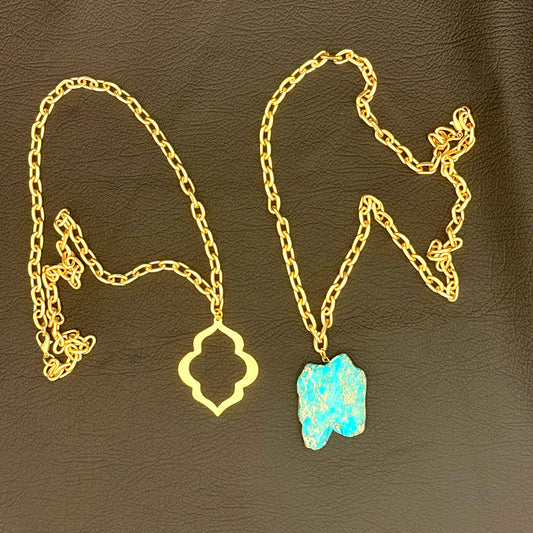 Two gold chain necklaces displayed on a dark brown textured surface. One necklace features a gold quatrefoil pendant, and the other features a turquoise blue stone pendant.