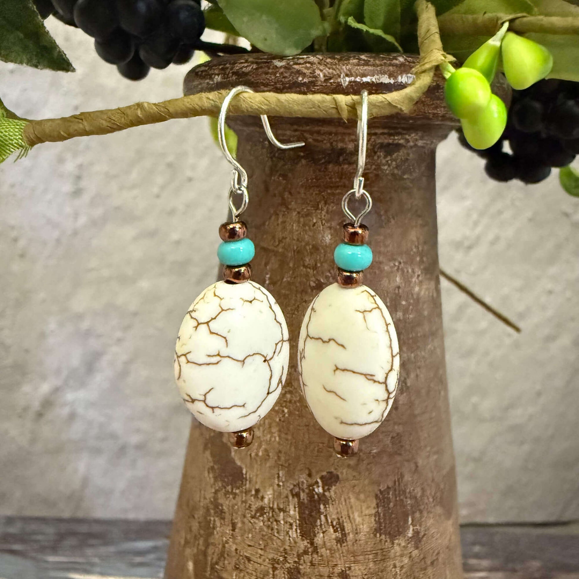 Pair of earrings with white beads and turquoise accents hanging on a wooden stand.