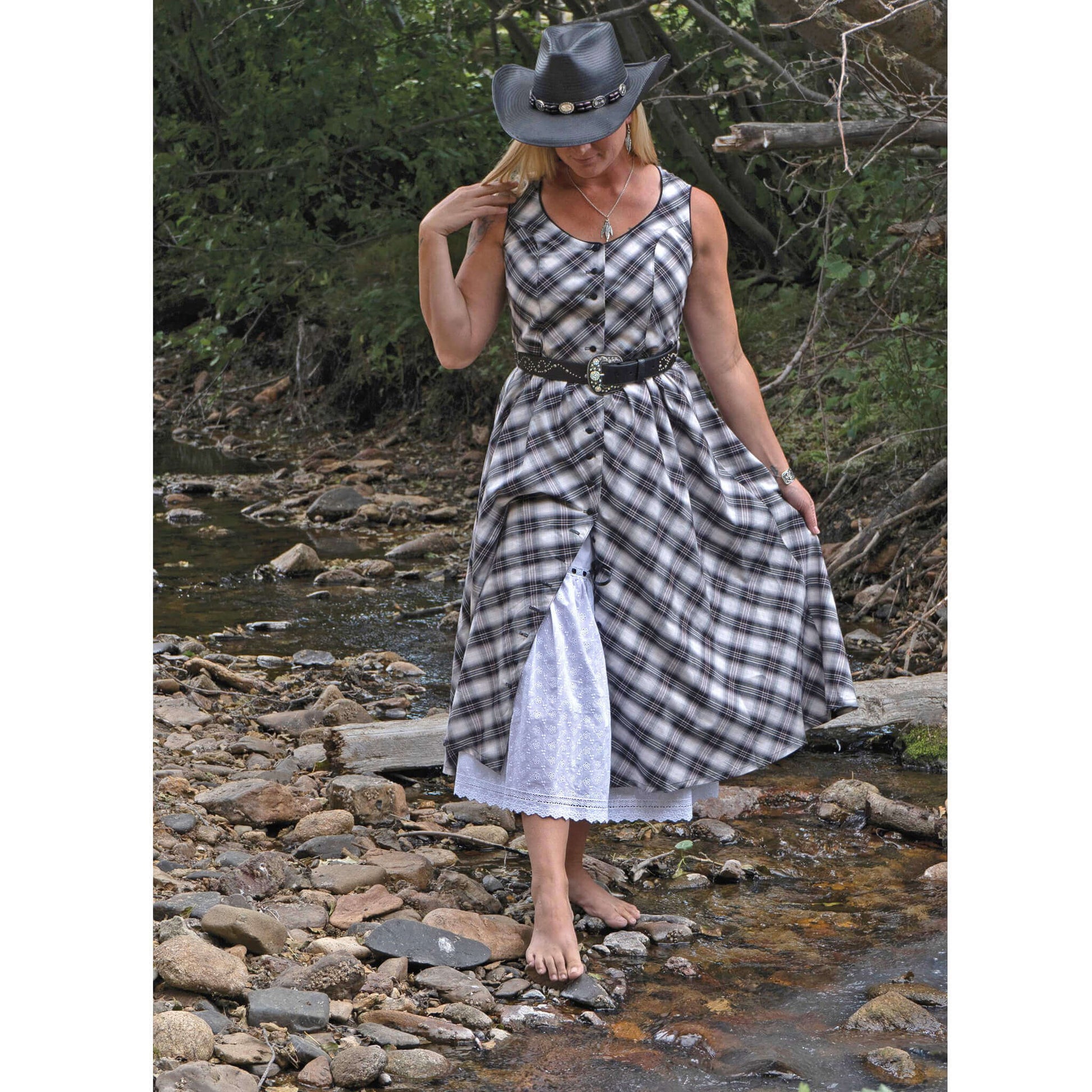 Woman in Scottsdale Sleeveless Western Summer Dress by creek, featuring plaid design and eyelet petticoat.