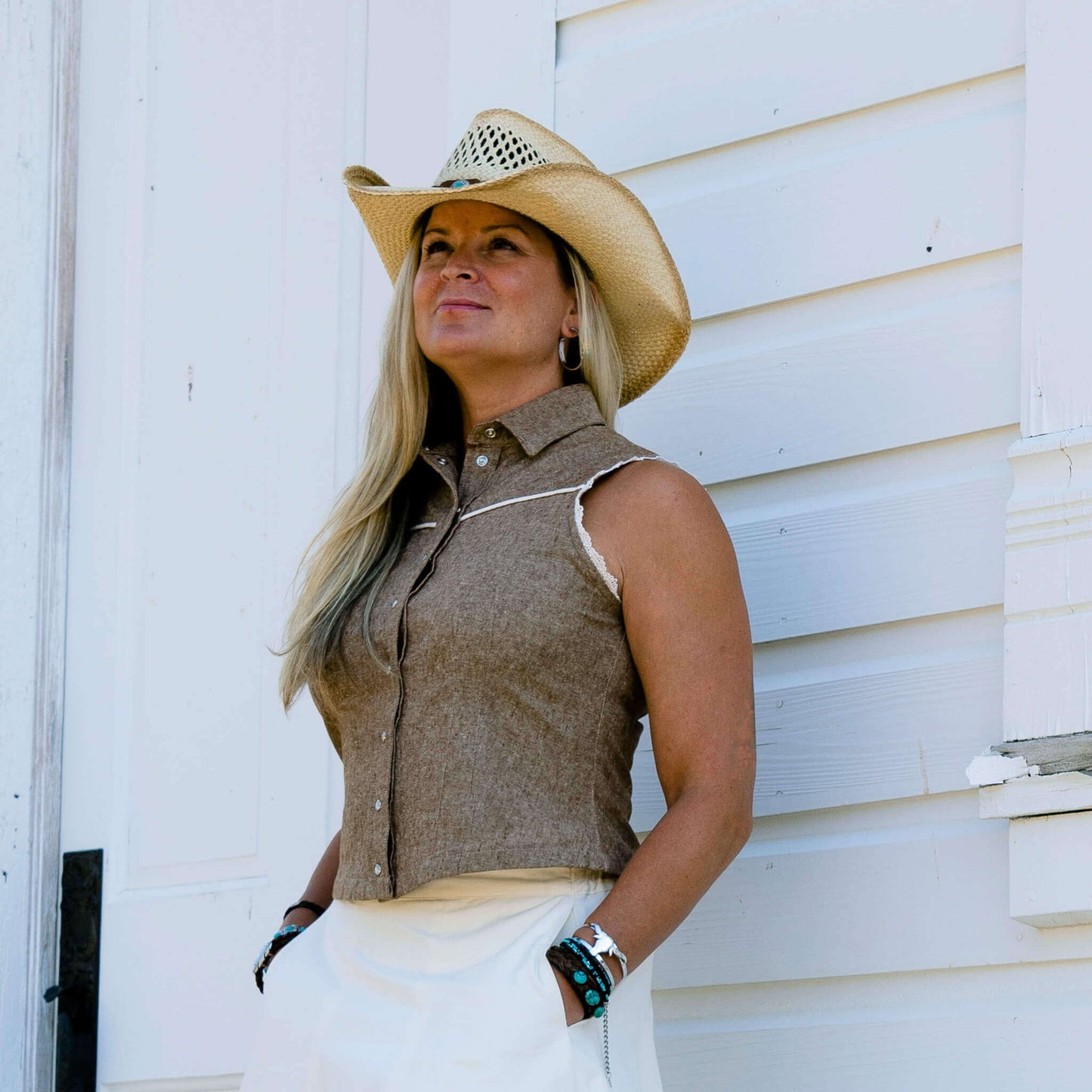 Woman wearing Sierra Rodeo Cowgirl Blouse and cowboy hat against a rustic white backdrop.