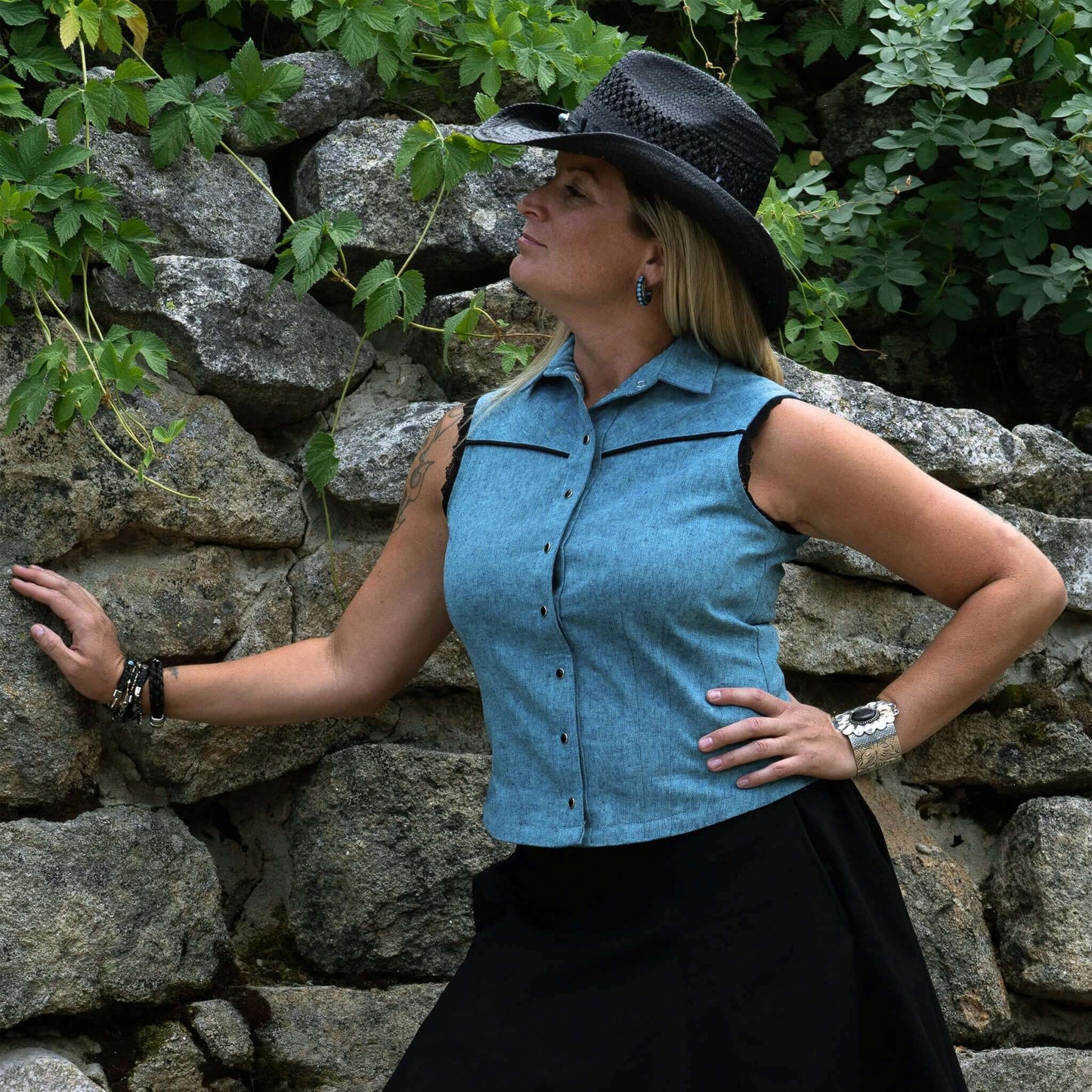 Woman modeling a Sierra Rodeo Cowgirl Blouse against a stone wall, showcasing western style and lace details.