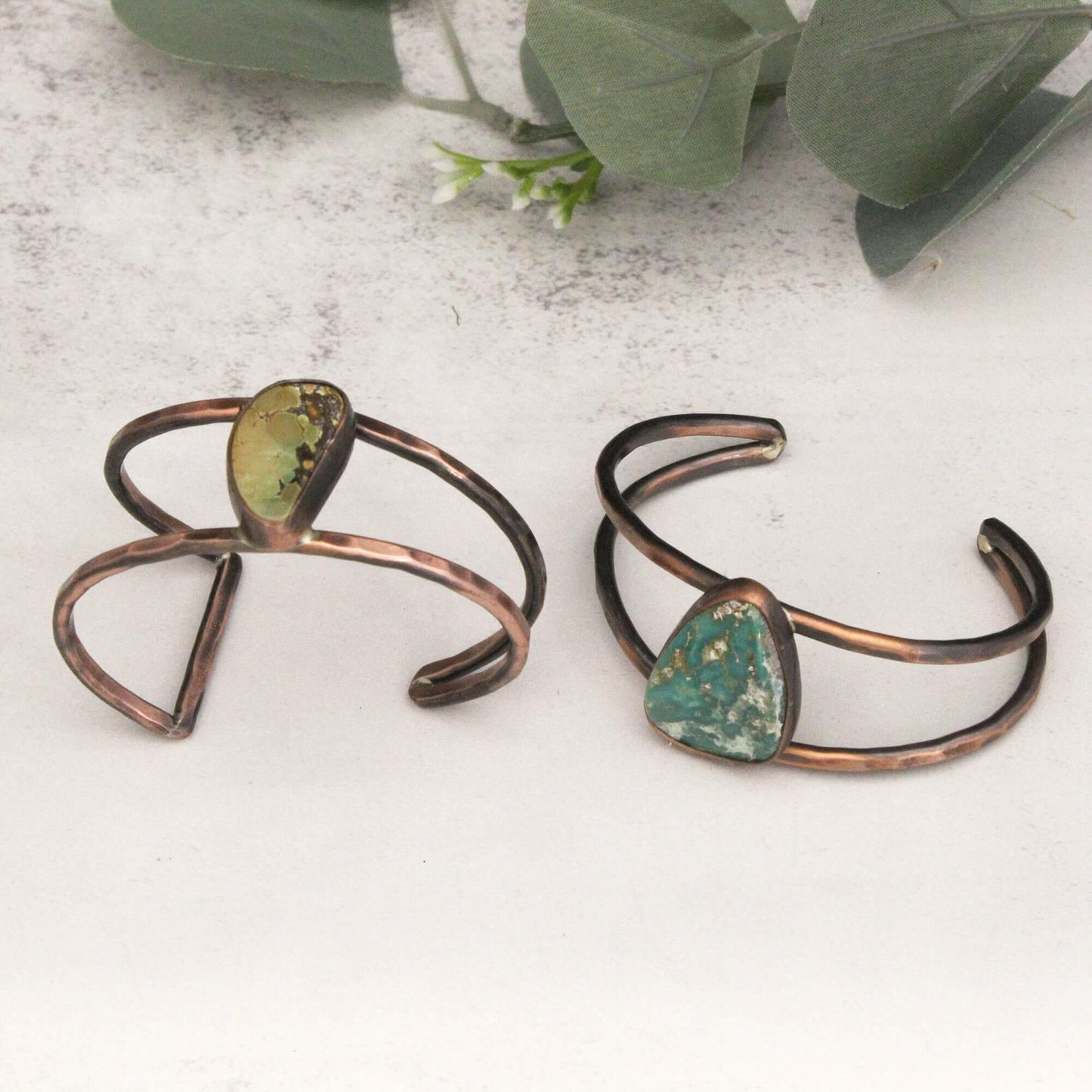 Two copper bracelets with green stone accents on a light surface.