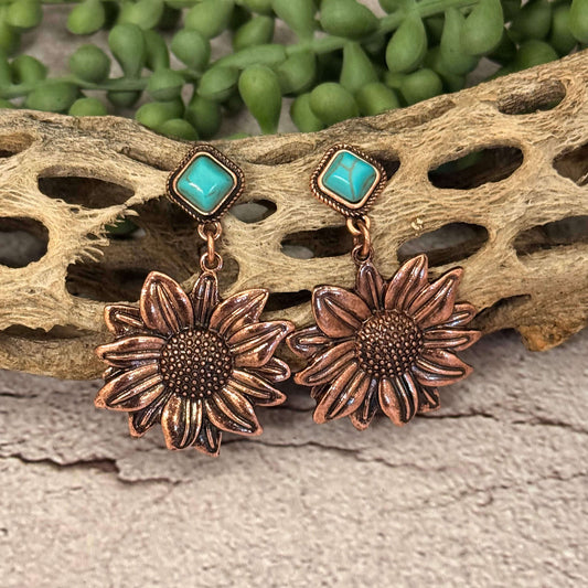 Copper sunflower earrings with turquoise stones on a natural wood and green plant background