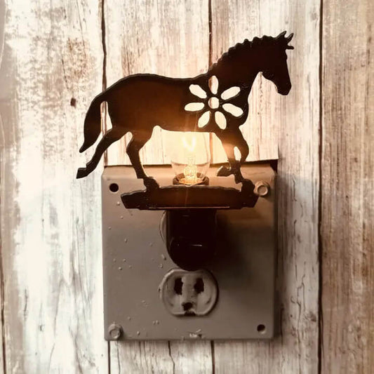 A rustic metal night light shaped like a horse with a flower cutout, mounted on a wall outlet against a weathered wood plank background.