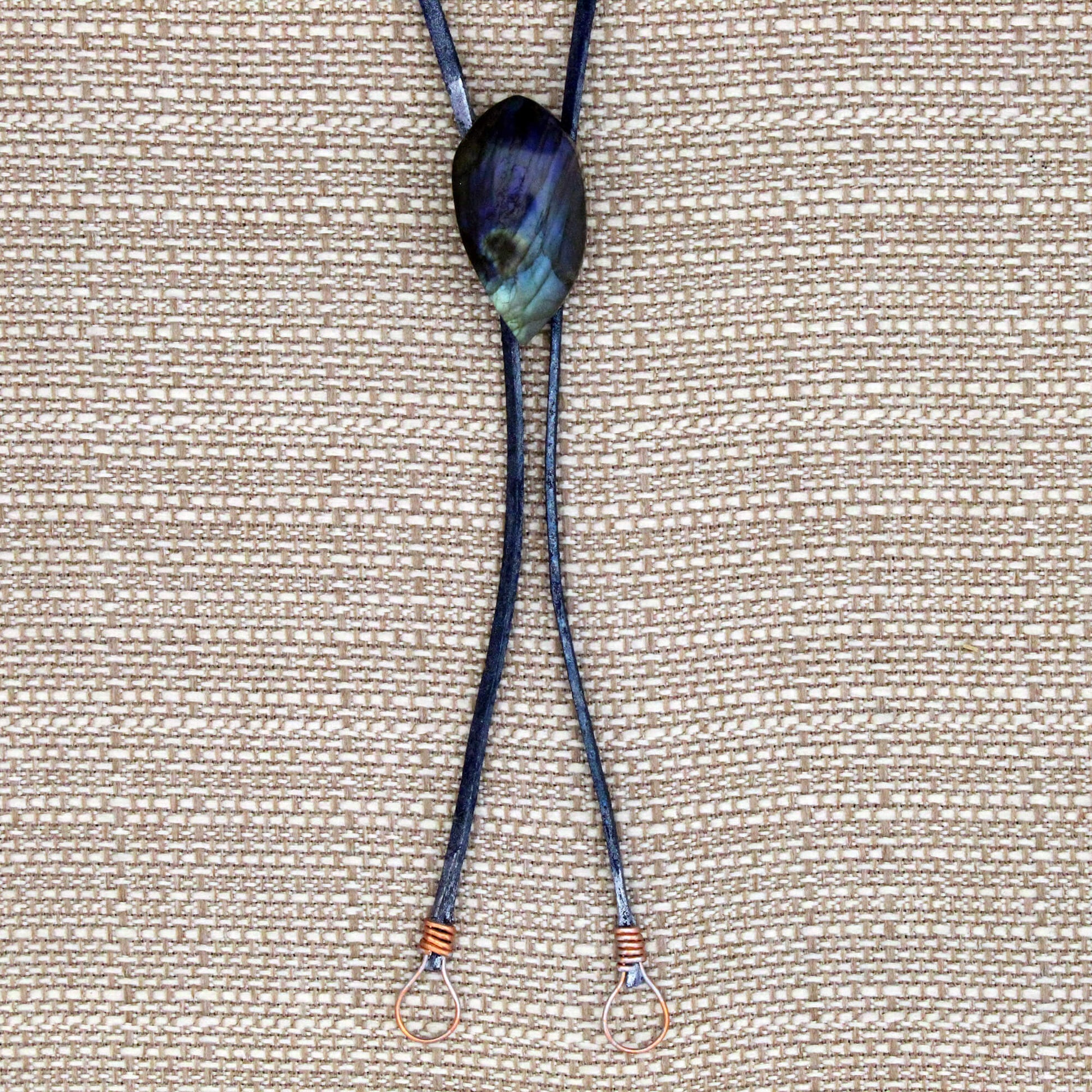 Bolo Tie with a dark blue cord and a large, multicolored stone pendant on a beige fabric background.