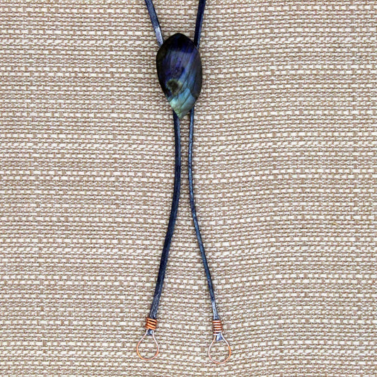 Bolo Tie with a dark blue cord and a large, multicolored stone pendant on a beige fabric background.
