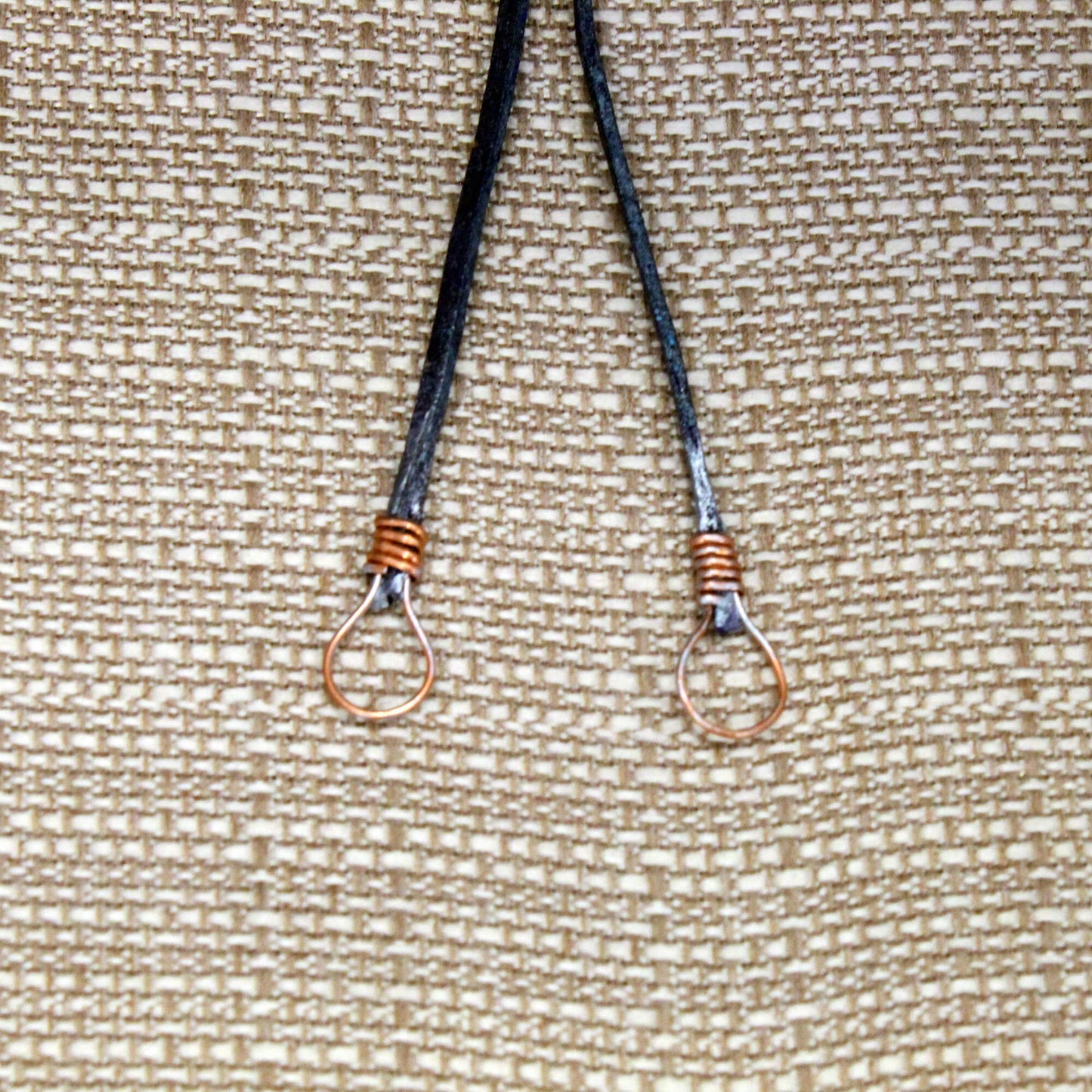 Two black lanyards with metal hooks on a textured beige background