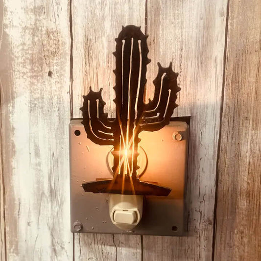 A rustic metal cactus night light mounted on a weathered wood plank wall, glowing with a warm light from within.