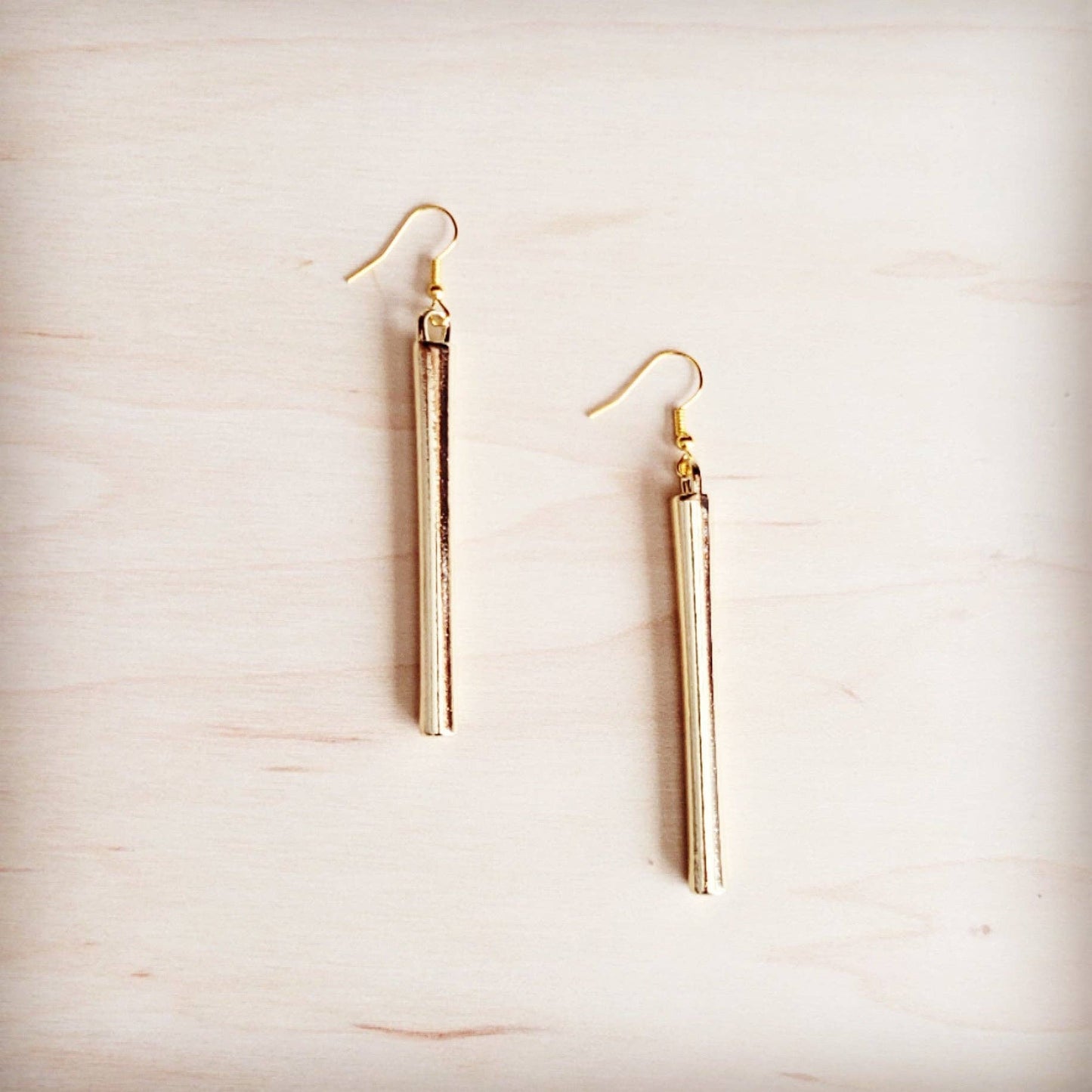 Gold tube earrings on a light wood surface
