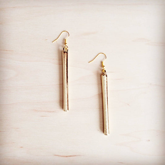 Gold tube earrings on a light wood surface