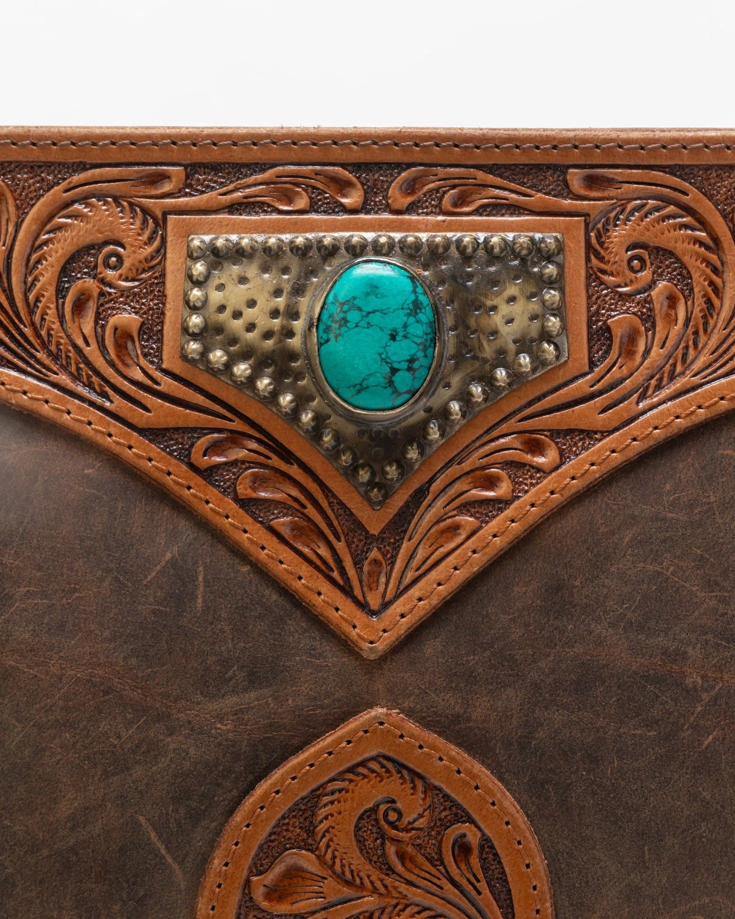 Close-up of a brown leather bag with intricate tooling and a turquoise stone.