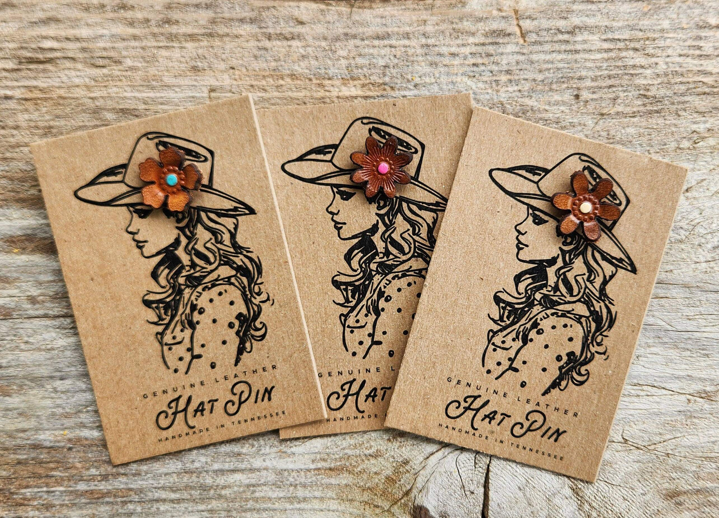 Three hat pins with decorative flowers on brown paper packaging against a wooden background