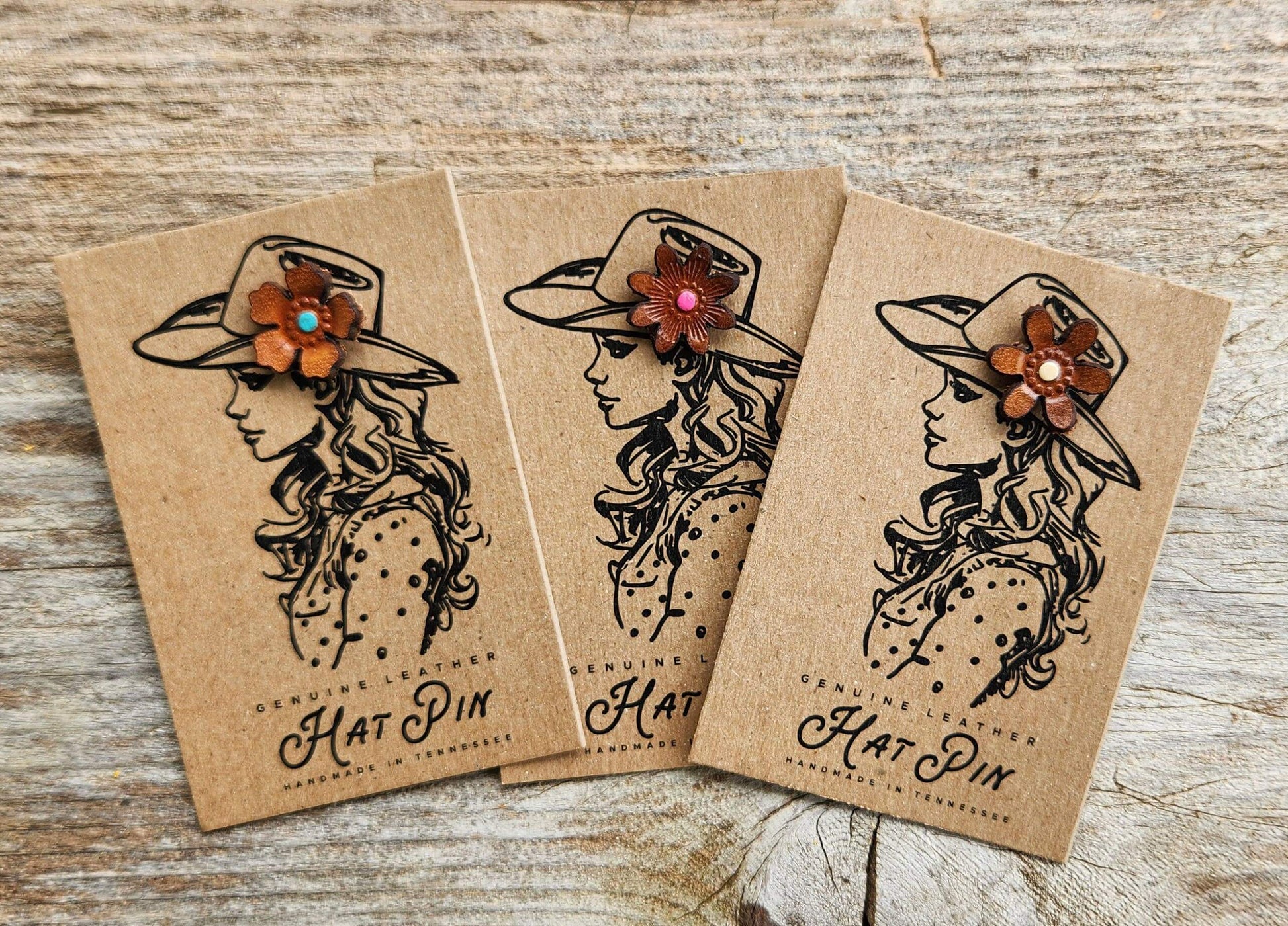 Three hat pins with decorative flowers on brown paper packaging against a wooden background