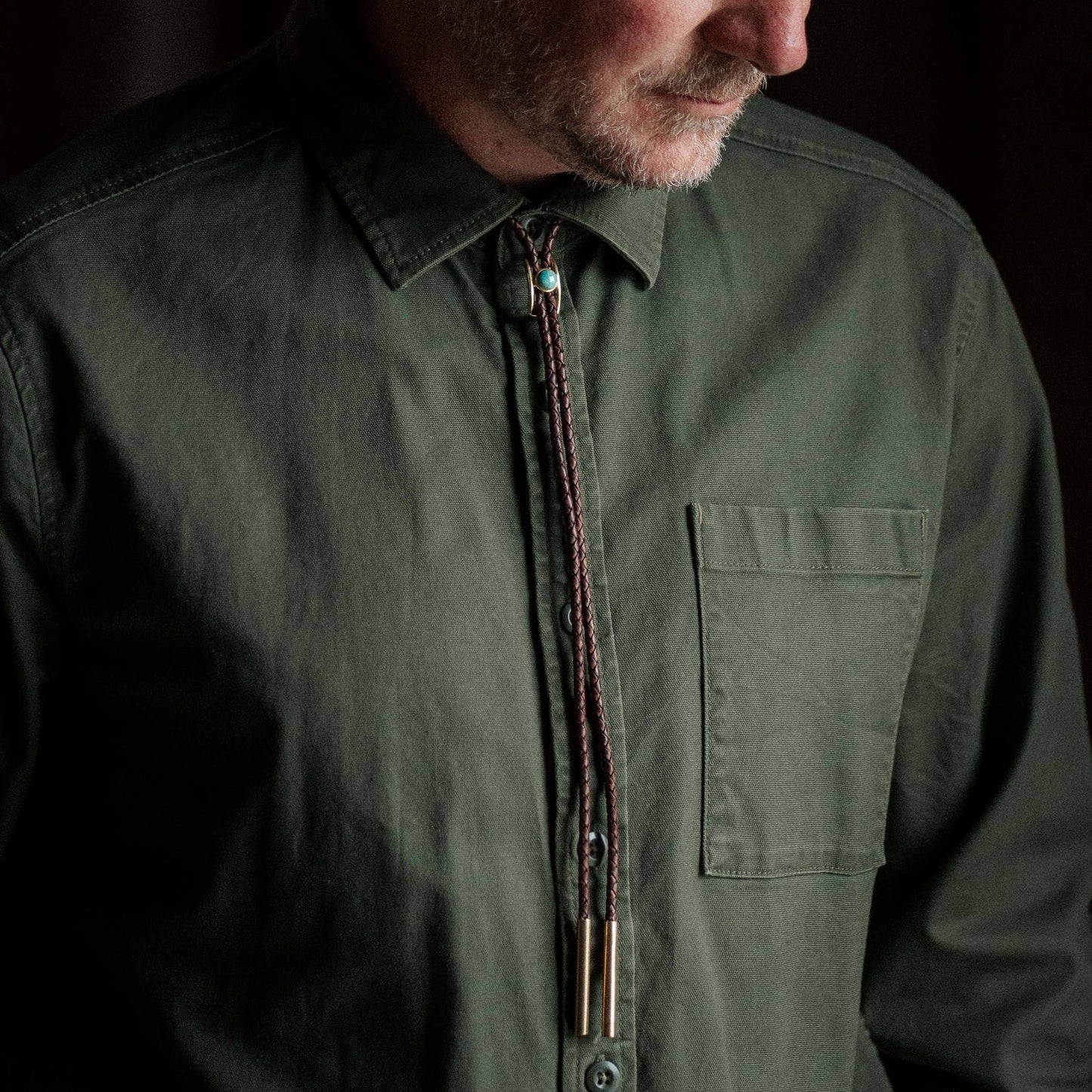 Man wearing a green shirt with a bolo tie against a dark background