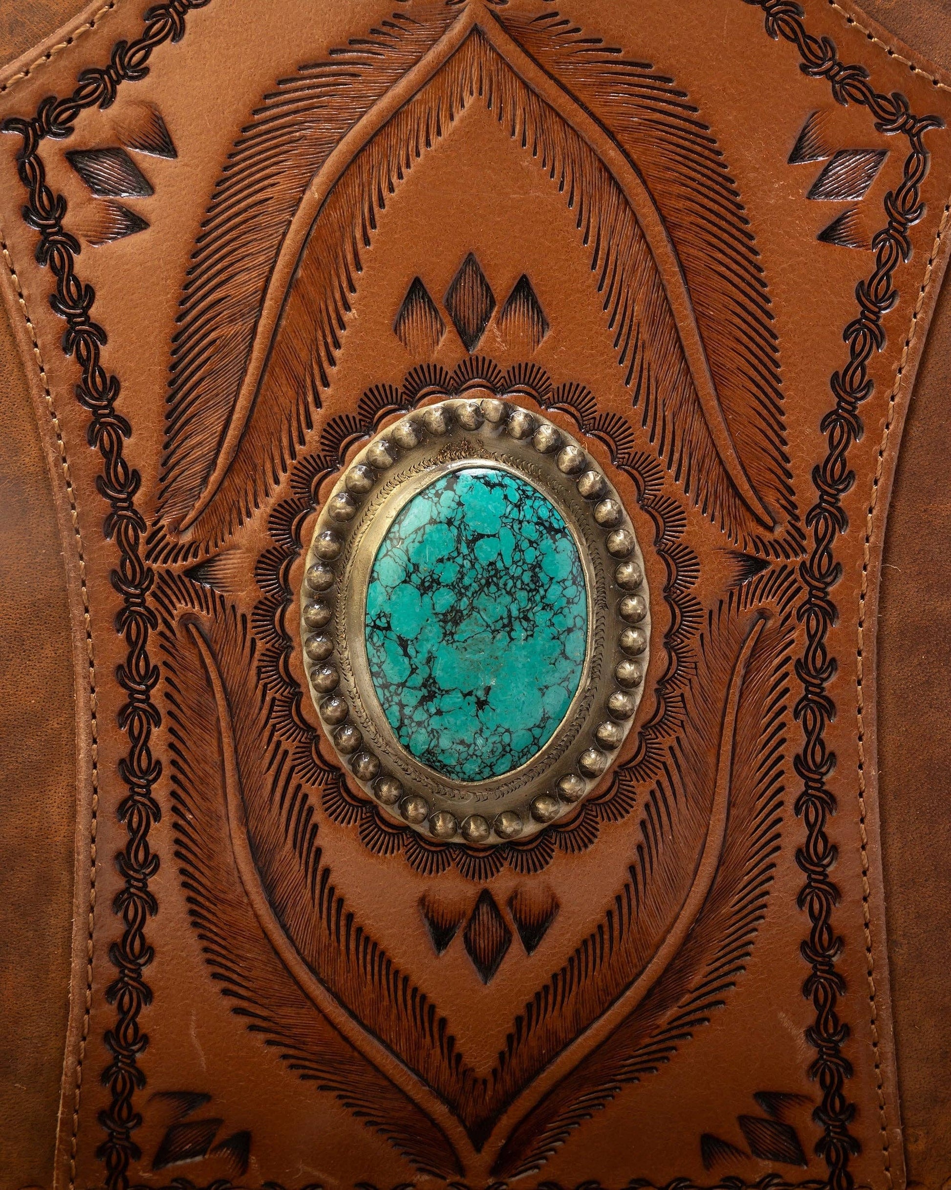 Close-up of a leather product with intricate embossing and a turquoise stone in the center.