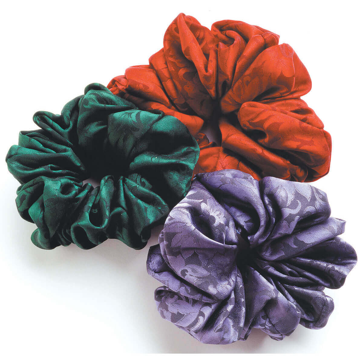 Three colorful scrunchies in red, green, and purple on a white background