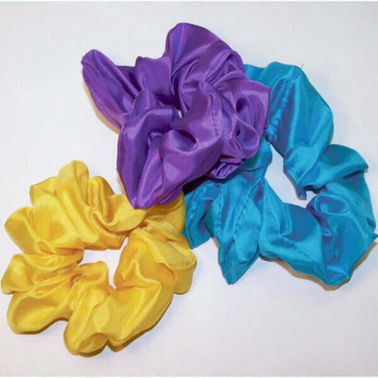 Three silk scrunchies in purple, yellow, and blue on a white background